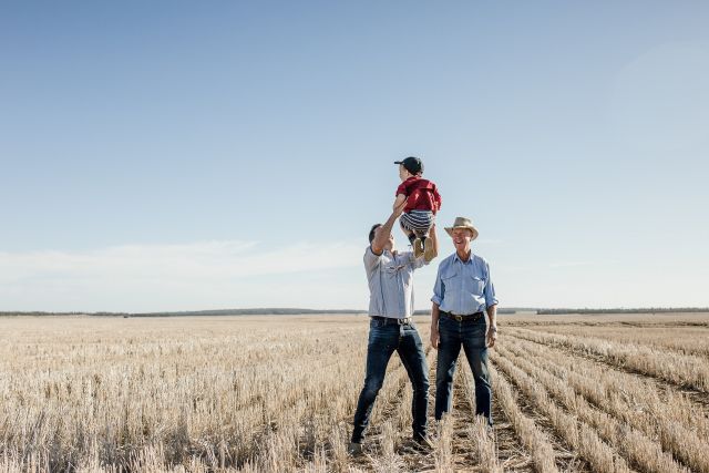 Two men standing in a field of crops. One man holding a small child.
