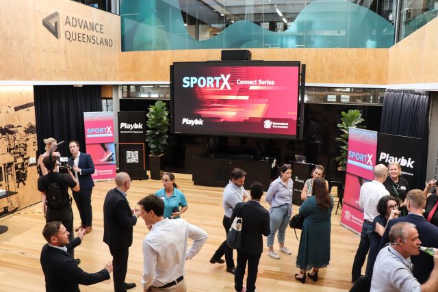 Group of 17 people mingling in a room with a SportX logo in the background on a large screen