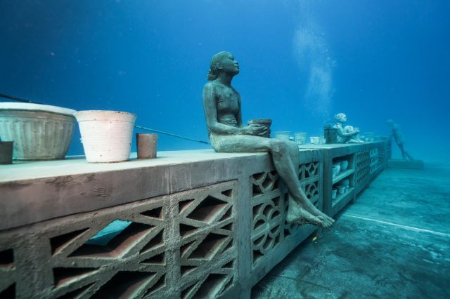 Concrete wall with sculptures of girls holding buckets sitting on the wall. All of this underwater